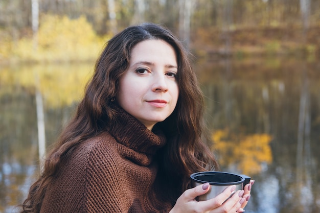 Chica bebiendo té en un puente de madera sobre un lago