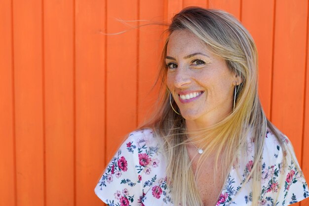 Chica de belleza de sonrisa en mujer de verano con largos pelos rubios en fondo de madera naranja