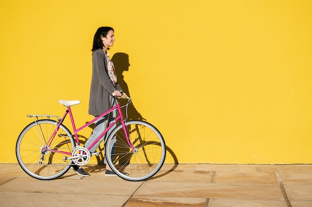 Chica con una bicicleta caminando delante de la pared amarilla