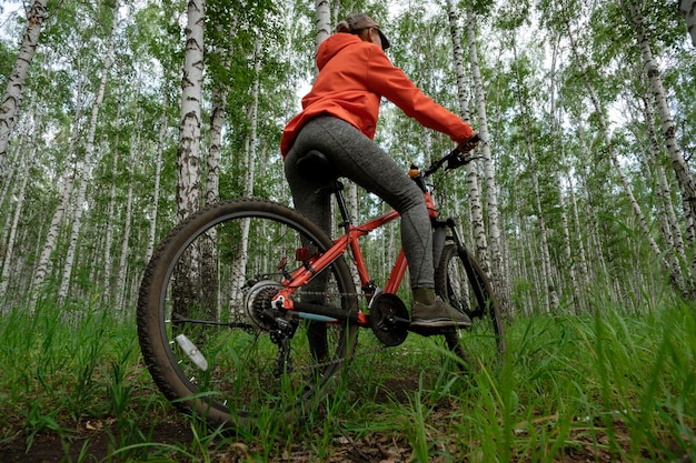Chica en una bicicleta hermosa wonam en una chaqueta naranja brillante en una bicicleta en el bosque