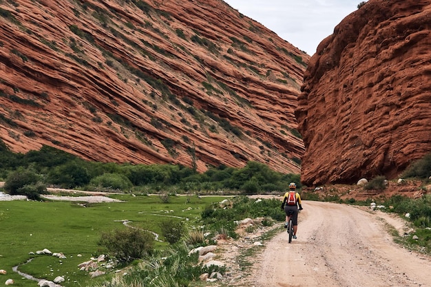 Foto chica en bicicleta a lo largo de la asombrosa cordillera roja de jeti oguz seven bulls rock canyon kirguistán