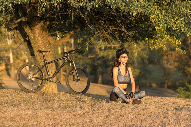 Chica en bicicleta de montaña en campo a través, hermoso retrato de un ciclista al atardecer, Chica fitness monta una bicicleta de montaña de fibra de carbono moderna en ropa deportiva. Primer plano, retrato, de, un, niña, en, un, casco, y, anteojos