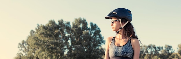 Chica en bicicleta de montaña en campo a través hermoso retrato de un ciclista al atardecer Chica fitness monta una bicicleta de montaña moderna de fibra de carbono en ropa deportiva Retrato de una niña con casco y gafas