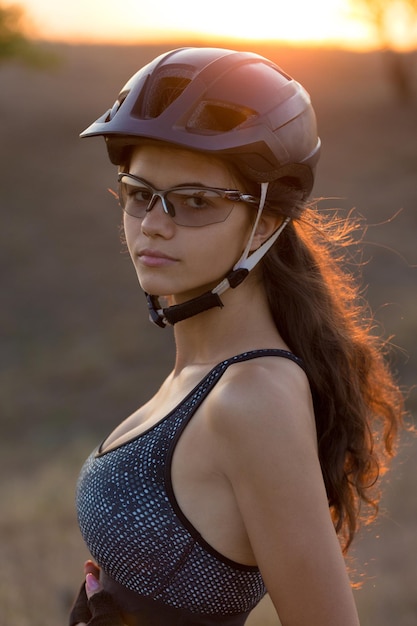 Chica en bicicleta de montaña en campo a través hermoso retrato de un ciclista al atardecer Chica fitness monta una bicicleta de montaña moderna de fibra de carbono en ropa deportiva