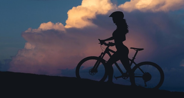 Chica en bicicleta de montaña en campo a través hermoso retrato de un ciclista al atardecer Chica fitness monta una bicicleta de montaña moderna de fibra de carbono en ropa deportiva