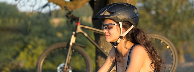 Chica en una bicicleta de montaña en campo a través, hermoso retrato de un ciclista al atardecer