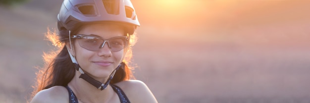Chica en una bicicleta de montaña en campo a través, hermoso retrato de un ciclista al atardecer