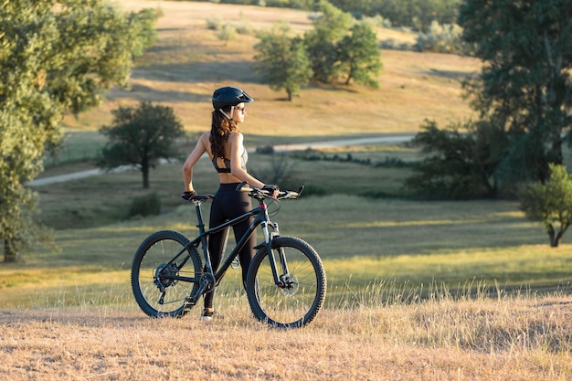 Chica en bicicleta de montaña en campo a través hermoso retrato de un ciclista al atardecer