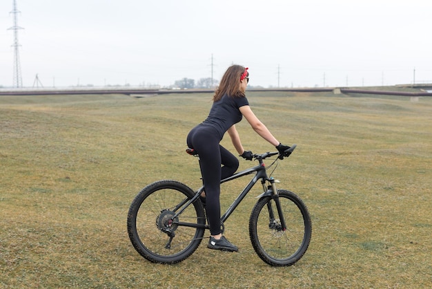 Chica en bicicleta de montaña en campo a través hermoso retrato de un ciclista en clima lluvioso Chica fitness monta una bicicleta de montaña moderna de fibra de carbono en ropa deportiva Retrato de detalle de una chica en pañuelo rojo