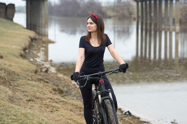 Chica en bicicleta de montaña en campo a través hermoso retrato de un ciclista en clima lluvioso Chica fitness monta una bicicleta de montaña moderna de fibra de carbono en ropa deportiva Retrato de una niña en pañuelo rojo