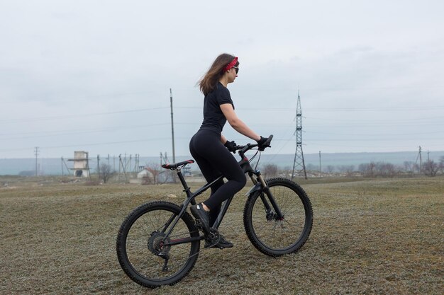 Chica en bicicleta de montaña en campo a través hermoso retrato de un ciclista en clima lluvioso Chica fitness monta una bicicleta de montaña moderna de fibra de carbono en ropa deportiva Retrato de una niña en pañuelo rojo