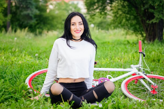 Chica en una bicicleta roja y blanca. Una muchacha atlética bronceada atractiva bastante joven monta en naturaleza. Alegre y sonriente morena. buenas cifras