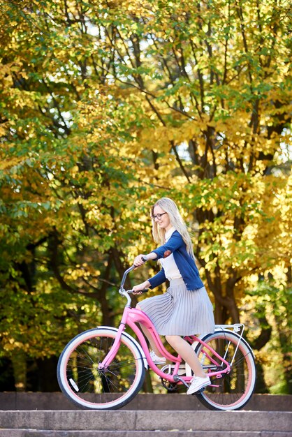 Chica en bicicleta rosa en el soleado parque de otoño