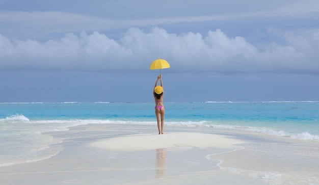 chica en bikini con un paraguas amarillo en la arena del mar