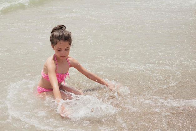 Chica en bikini rosa jugando alegremente en la orilla de la playa con las olas en un día soleado de verano Vera España