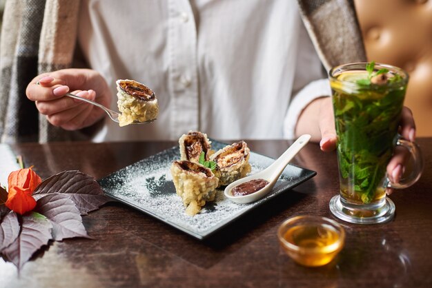 Chica en blanco sosteniendo una bebida comiendo sushi dulce.