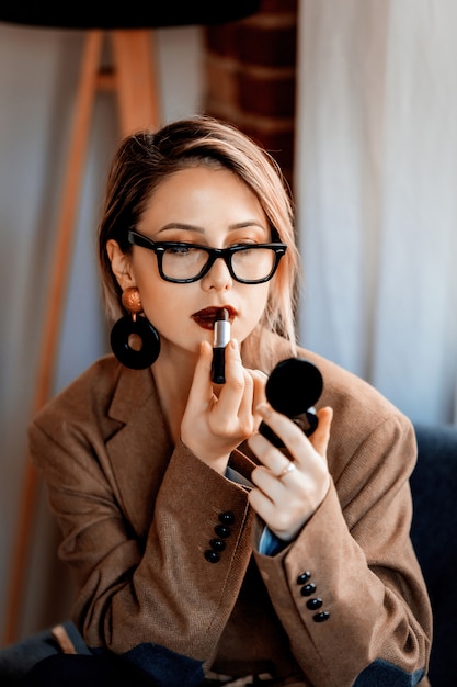 chica en blazer y gafas aplicando maquillaje