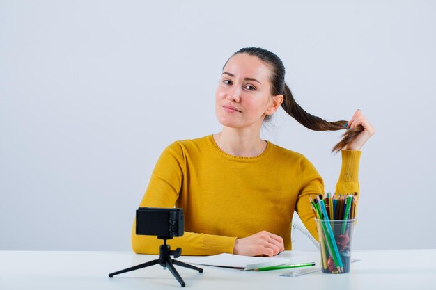 Chica blogger está mirando a la cámara sosteniendo el pelo sobre fondo blanco.