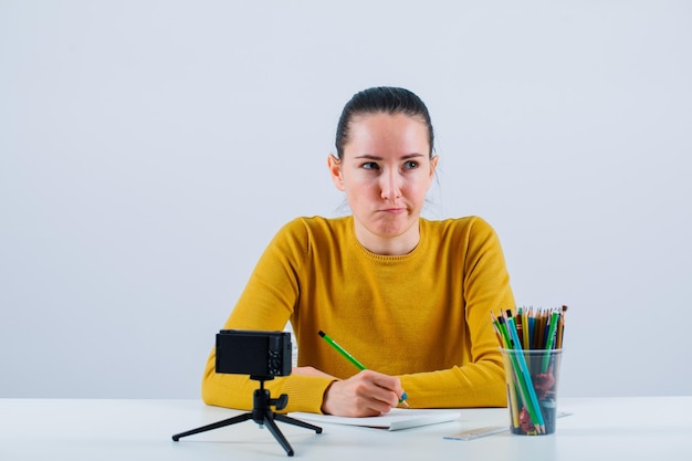 Chica blogger está pensando sosteniendo un lápiz sobre fondo blanco.