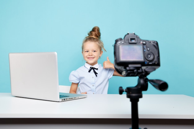 Chica blogger grabando vlog en la cámara sentado frente a la computadora en el estudio azul