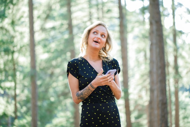 Chica bloguera está mirando hacia arriba sosteniendo el móvil en el fondo de la naturaleza