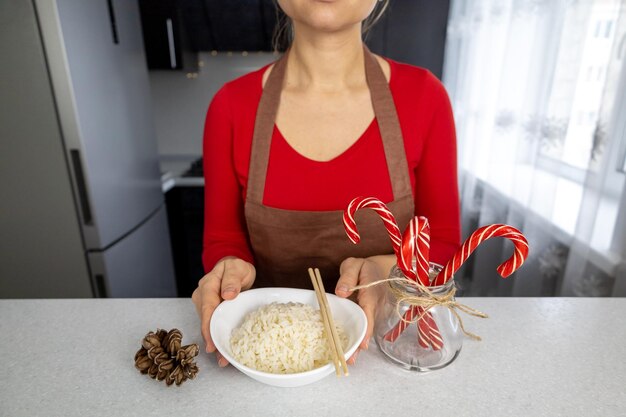 Una chica con una blusa roja y un delantal marrón sostiene un plato de arroz dorado en sus manos en una cocina oscura