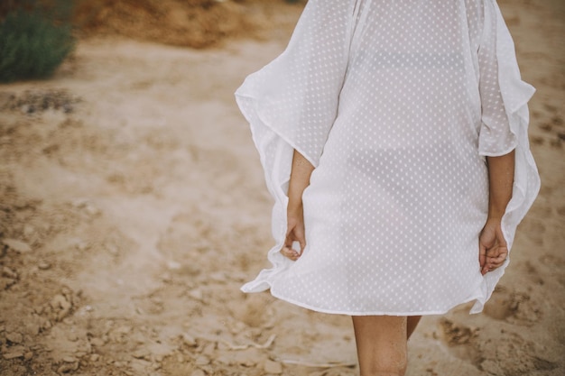 Foto chica boho despreocupada en vestido blanco de verano caminando en la playa vista posterior mujer joven en movimiento relajarse en la orilla del mar vacaciones de verano conciencia y relajación estilo de vida