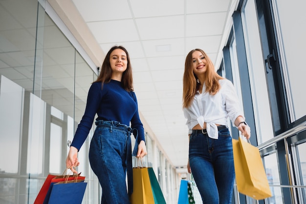 Chica con bolsas caminando con su novia en el centro comercial y de compras