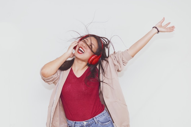 Foto chica bonita asiática escuchando música con auriculares rojos sobre fondo blanco.