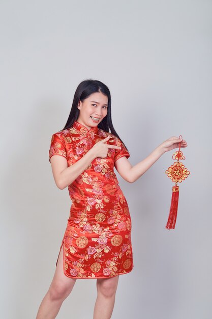 Chica bonita asiática con vestido tradicional chino cheongsam o qipao sosteniendo petardo. Concepto de año nuevo chino, modelo femenino aislado en fondo gris de estudio