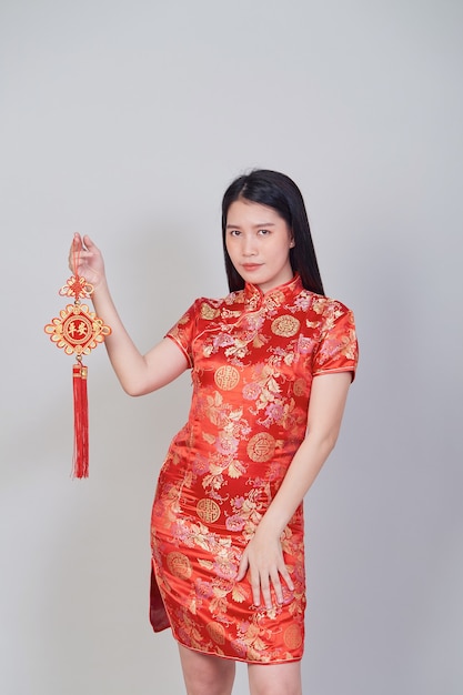 Chica bonita asiática con vestido tradicional chino cheongsam o qipao sosteniendo petardo. Concepto de año nuevo chino, modelo femenino aislado en fondo gris de estudio