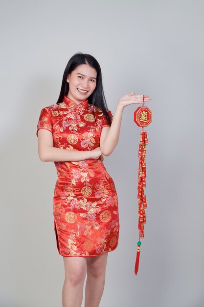 Chica bonita asiática con vestido tradicional chino cheongsam o qipao sosteniendo petardo. Concepto de año nuevo chino, modelo femenino aislado en fondo gris de estudio