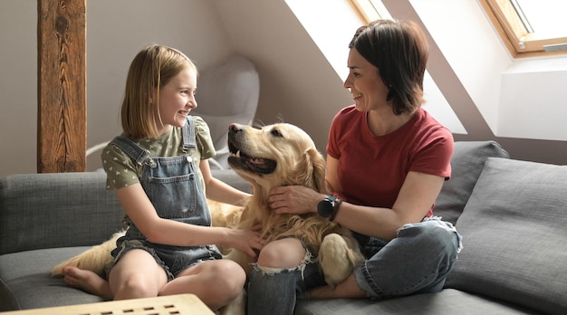 Chica bonita y niño preadolescente familia acariciar perro golden retriever sentado en el sofá madre y