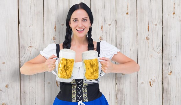 Chica bonita oktoberfest sosteniendo jarras de cerveza contra el fondo de madera