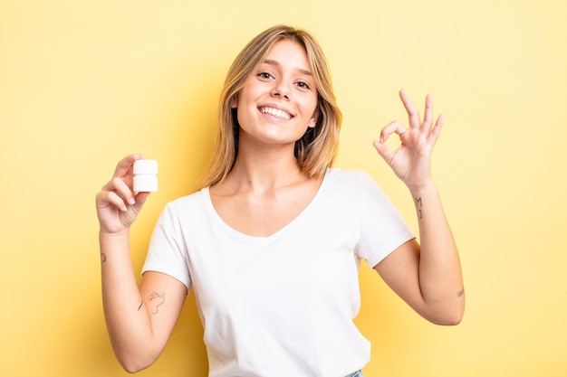 Chica bonita rubia que se siente feliz, mostrando aprobación con gesto bien. concepto de botella de pastillas