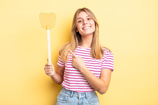 Chica bonita rubia sonriendo alegremente, sintiéndose feliz y apuntando hacia un lado. concepto de matar moscas