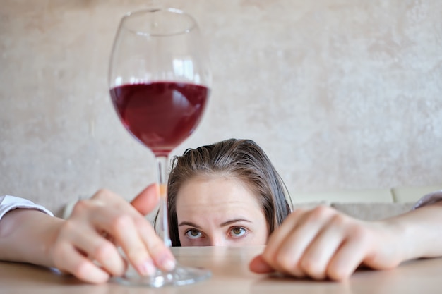 La chica borracha mira desde debajo de la mesa a una copa de vino.