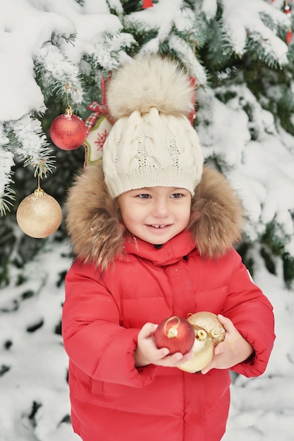 Chica en bosque de invierno. Bebé divertido que ríe al aire libre en día de invierno. Chica feliz invierno en la nieve del parque. Navidad en invierno bosque o parque.