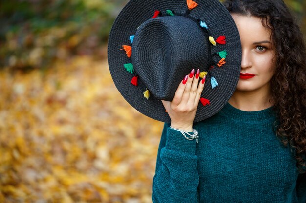 Chica en el bosque de otoño con un sombrero en sus manos