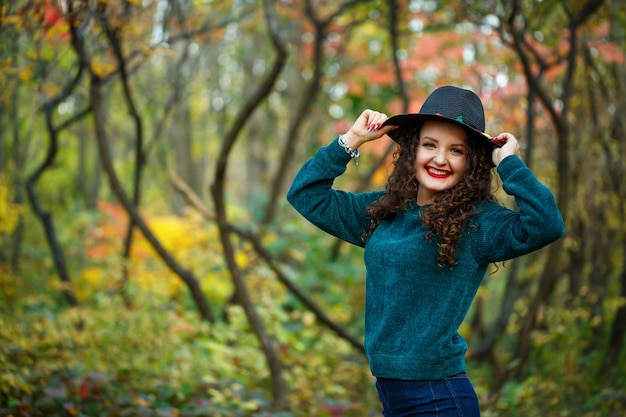 Chica en el bosque de otoño con un sombrero en sus manos