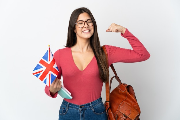 Chica brasileña adolescente sosteniendo una bandera de Reino Unido aislada en la pared blanca haciendo gesto fuerte