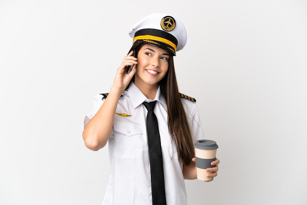 Chica brasileña piloto de avión sobre fondo blanco aislado sosteniendo café para llevar y un móvil