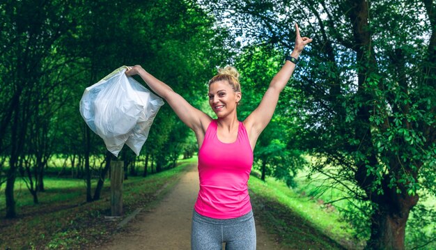 Chica brazos arriba mostrando bolsas de basura haciendo plogging