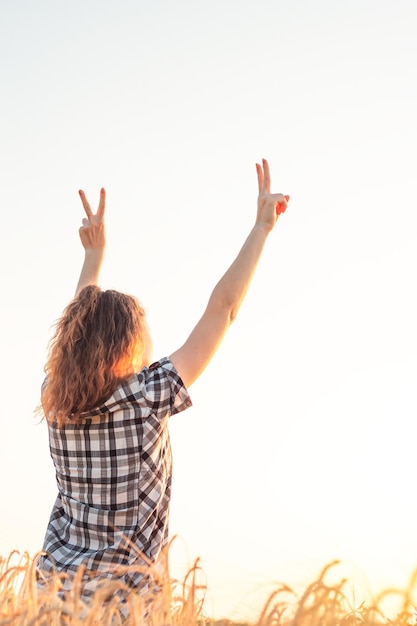 Chica con los brazos extendidos en un campo de trigo al atardecer