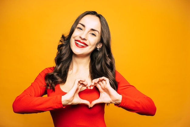 Chica brillante con una piel perfecta, cabello largo, suave y rizado y un lápiz labial rojo aterciopelado en sus labios carnosos lleva un suéter rojo a juego frente a un fondo llameante