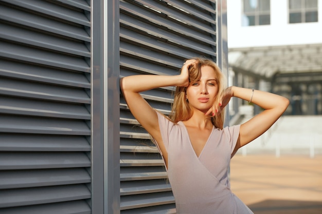 Chica bronceada de moda en vestido de moda posando en el fondo de las contraventanas metálicas. Espacio para texto