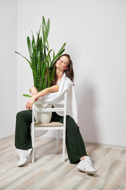 Chica bronceada con una planta verde sentada en una silla blanca