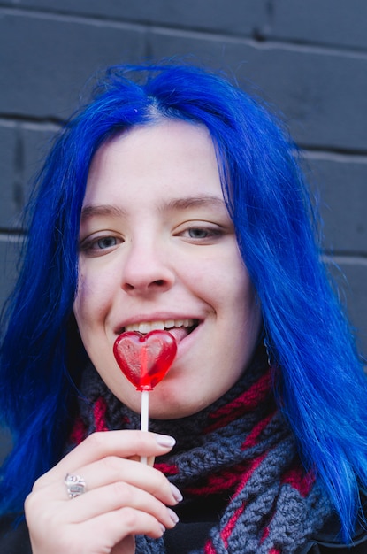 Chica con cabello azul con paletas de San Valentín en forma de corazón sobre fondo de pared de ladrillo negro