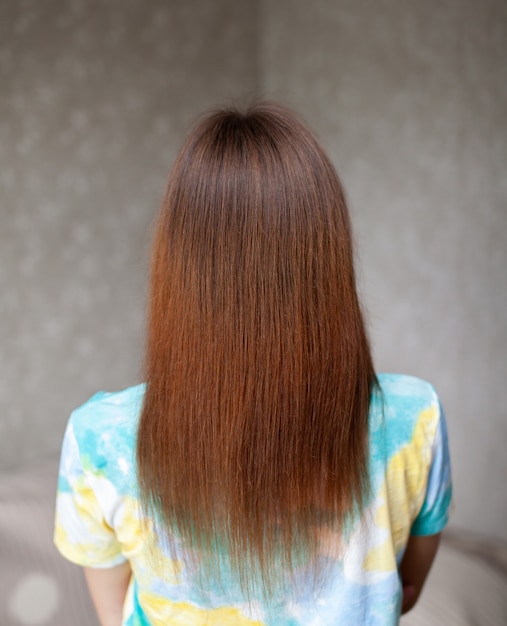 Una chica de cabello castaño largo, liso y hermoso. Cuidado del cabello en casa.