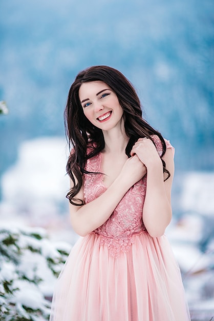 Chica con cabello castaño, ojos azules y un vestido rosa en el fondo de las montañas de invierno